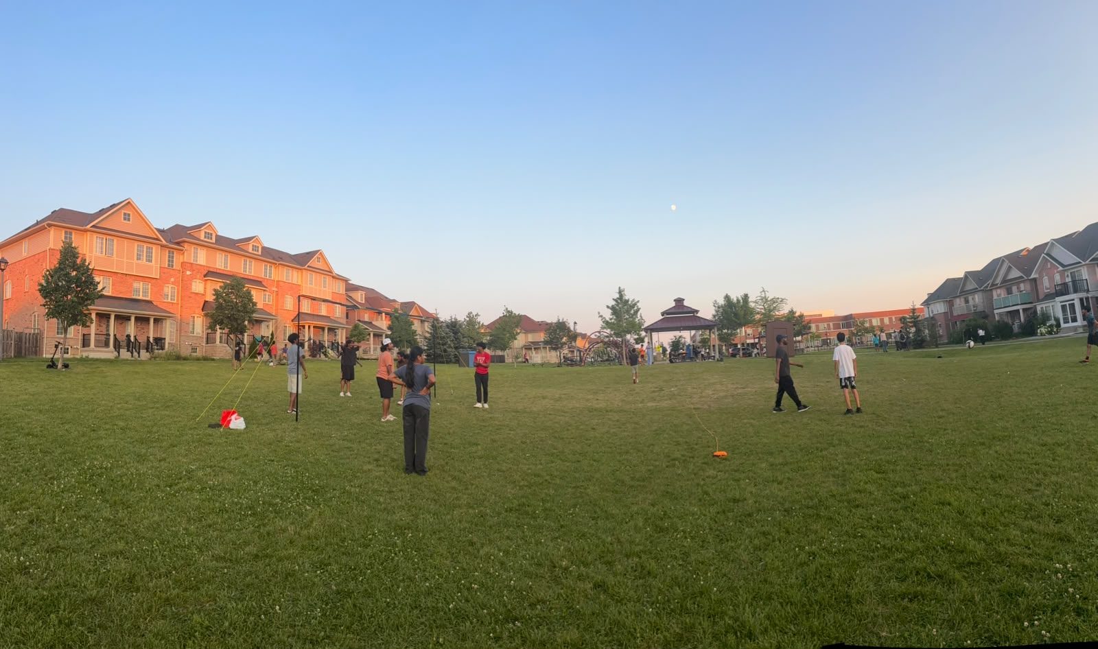 Sundial Park at dusk, families playing volleyball and cricket across the field